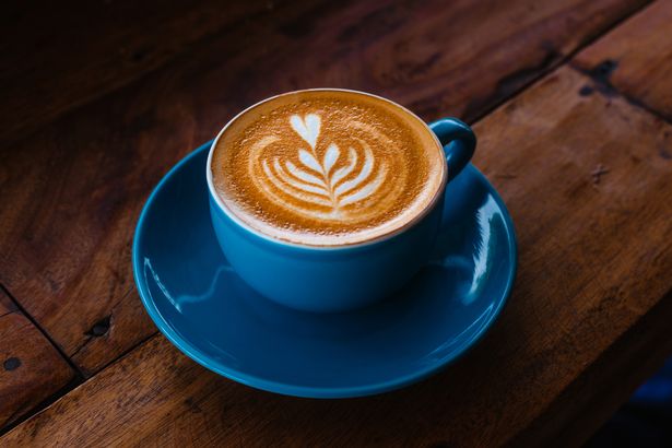 Cappuccino delicioso e perfumado com uma bela arte de café com leite em uma caneca de cerâmica azul em uma mesa de madeira. Café recém -fabricado de feijão assado. Publicidade elegante para sua cafeteria, restaurante e padaria