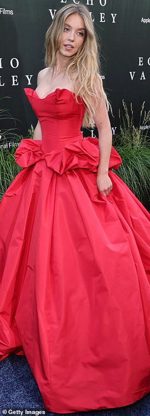 Seu luxuoso vestido escarlate foi apertado ao redor de sua barriga de middeciona envergonhada antes de fluir para uma saia luxuosa que fluía pelo chão